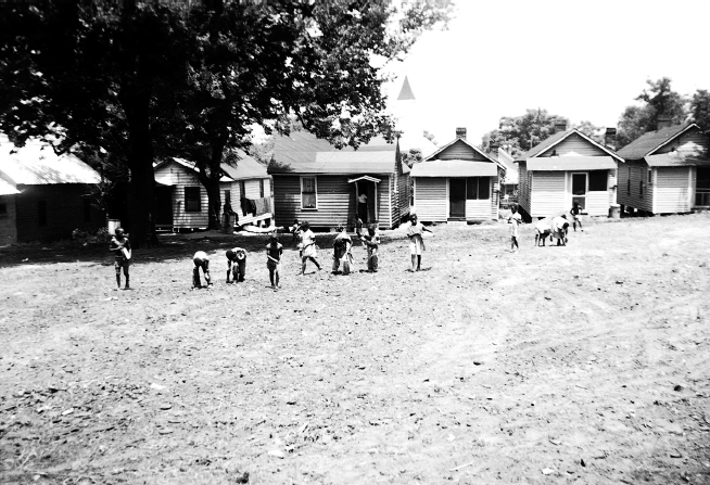 Twelve young children pick up debris in front of six modest homes.