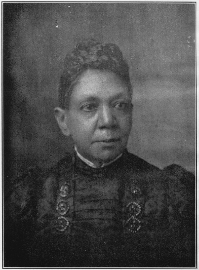 Formal bust portrait of a woman. She wears a dark jacquard dress and looks to the right side of the frame.