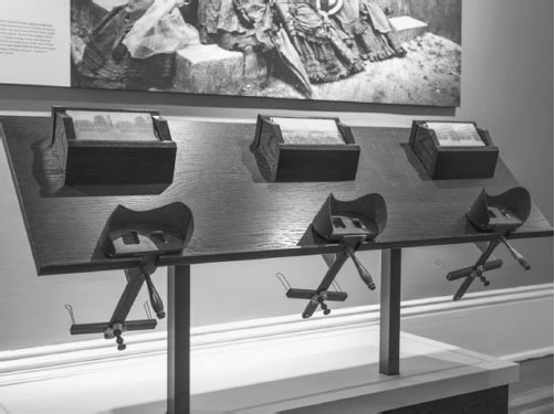 Three stereoscopes in a wooden display with corresponding photos to view with them.