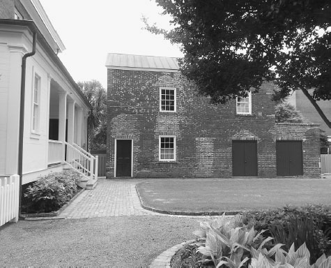 Back of a brick house with a single door to the left, three windows, and two sets of double doors to the right.