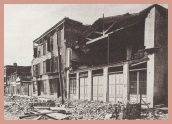 The damaged exterior of a two-story building. The surrounding area is covered in debris.