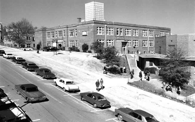 Brick school with cars and students in foreground.
