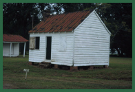 A small, white, clapboard building. Another similar structure is in the background.