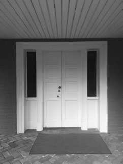 Two narrow white exterior doors with long windows on either side. A large mat rests in front of the doorway.