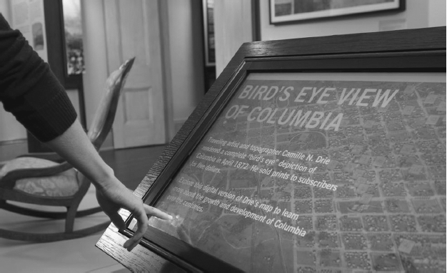 Touchscreen map and text in a wooden frame. A hand points to an area of the map.