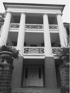 A close-up of the front of a painted brick three-story house, with grand white pillars and white fencing on two balconies.
