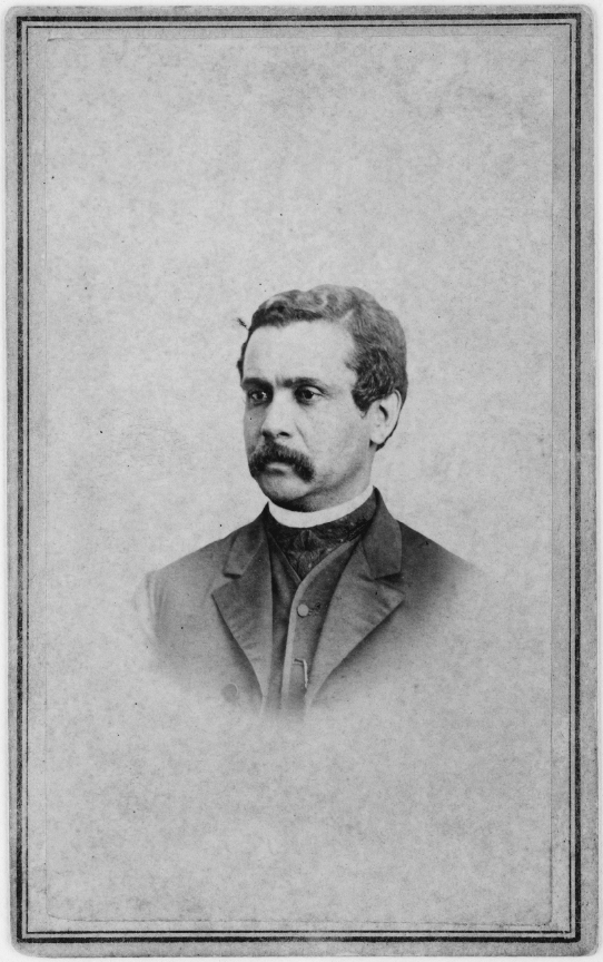 Head and shoulders of a man with a mustache, wearing a clerical collar and formal attire, facing to his right. 
