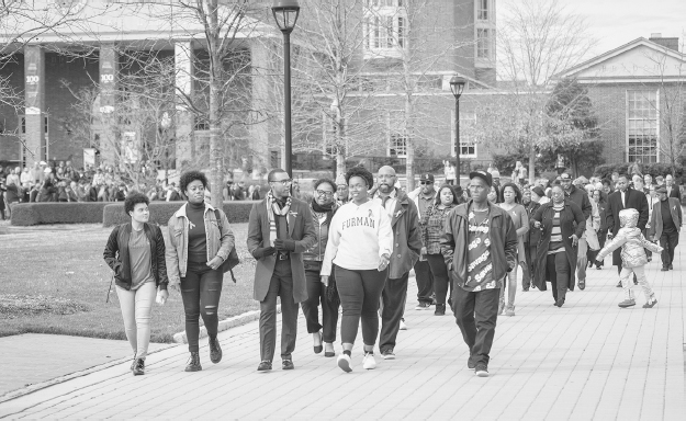 Figure 11. A large group of people march away from Joseph Vaughn Plaza with brick buildings in background.