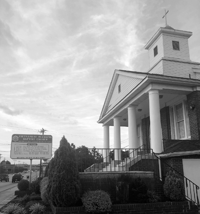 Brick building with stairs leading to a columned front porch with steeple above.