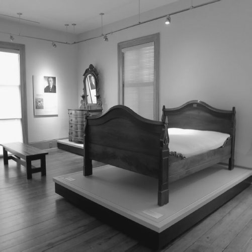 Staged bedroom furniture consisting of a wooden bed, bench seat, and vanity.