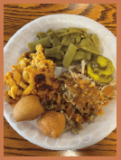 A meat served with three sides on a Styrofoam plate, including pulled pork, pickles, green beans, macaroni and cheese, and hush puppies.