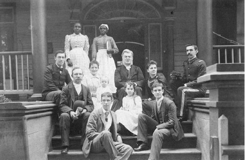 Group portrait of twelve people ranging from children to adults dressed up and posed on the front steps of a home.