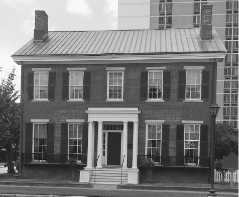Two-story brick house with dark shutters, white stairs leading to white columns, and two chimneys on the roof.