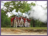 A group of people wearing Revolutionary-era clothing fire muskets.
