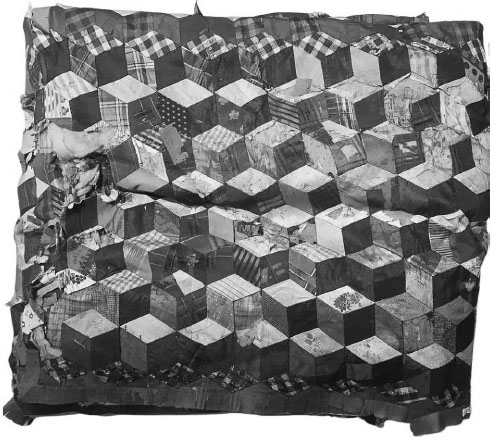 A patchwork quilt with worn edges, consisting of differing patterns and darker colors.
