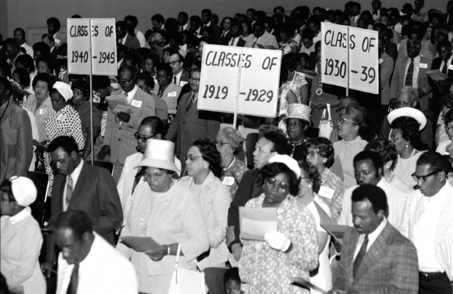People read programs and hold signs at high school reunion.