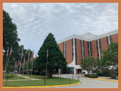 A large brick building with a manicured green space in front of it. There are several American flags on tall poles in the greenspace.