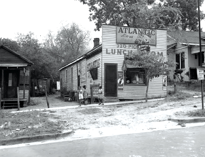 Three children stand on sidewalk near a restaurant with clapboard siding.