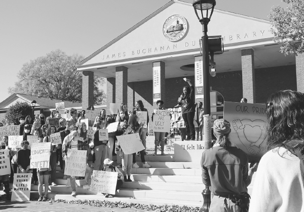 Figure 12. A group of students stand on Joseph Vaughn Plaza steps with protest signs and James B. Duke Library in background.